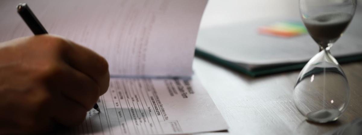 Person Filling Out Documents at a Desk with Passports and Hourglass-Shutterstock_2586825645